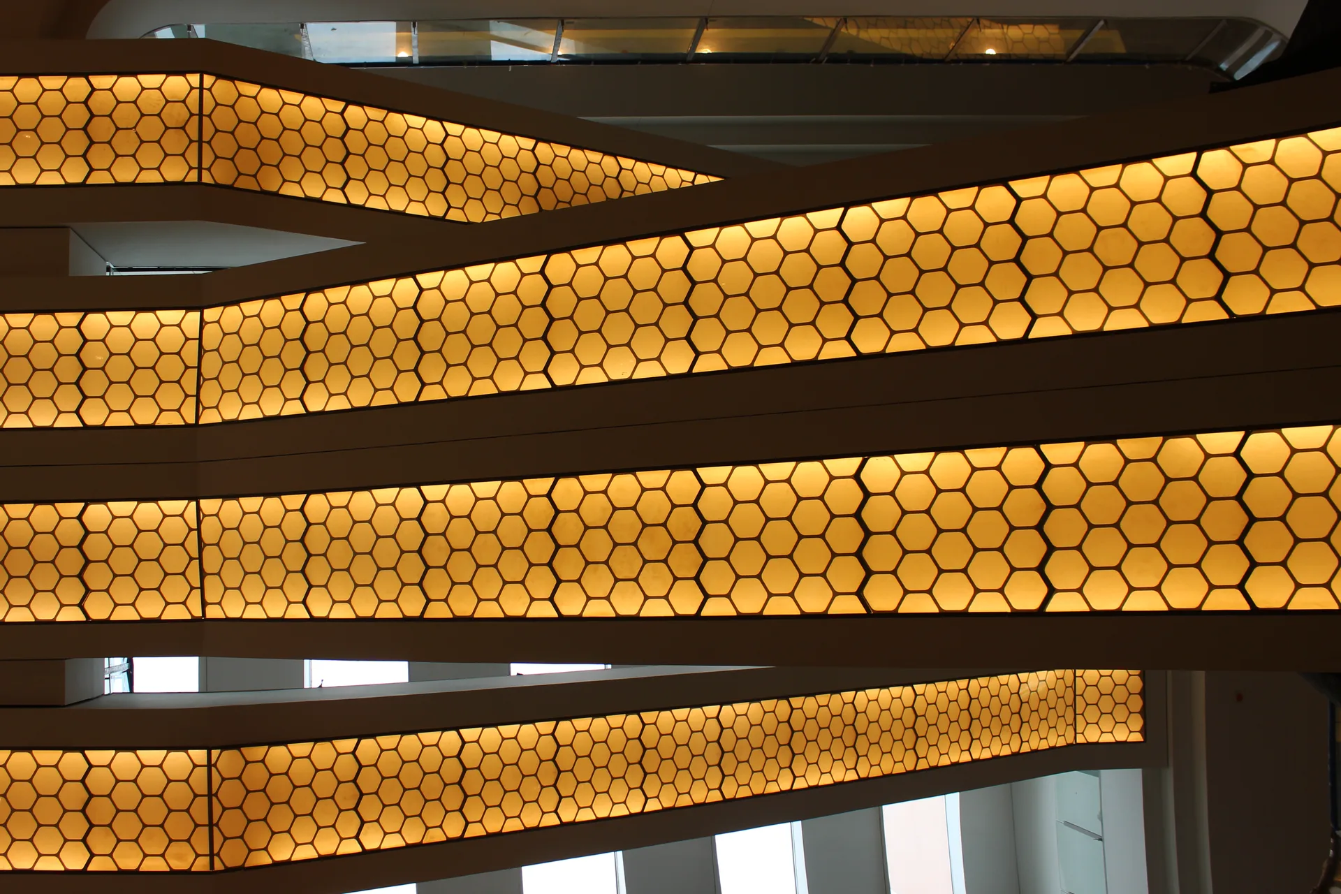 Backlit hexagonal-mesh balustrade panels seen against the atrium void