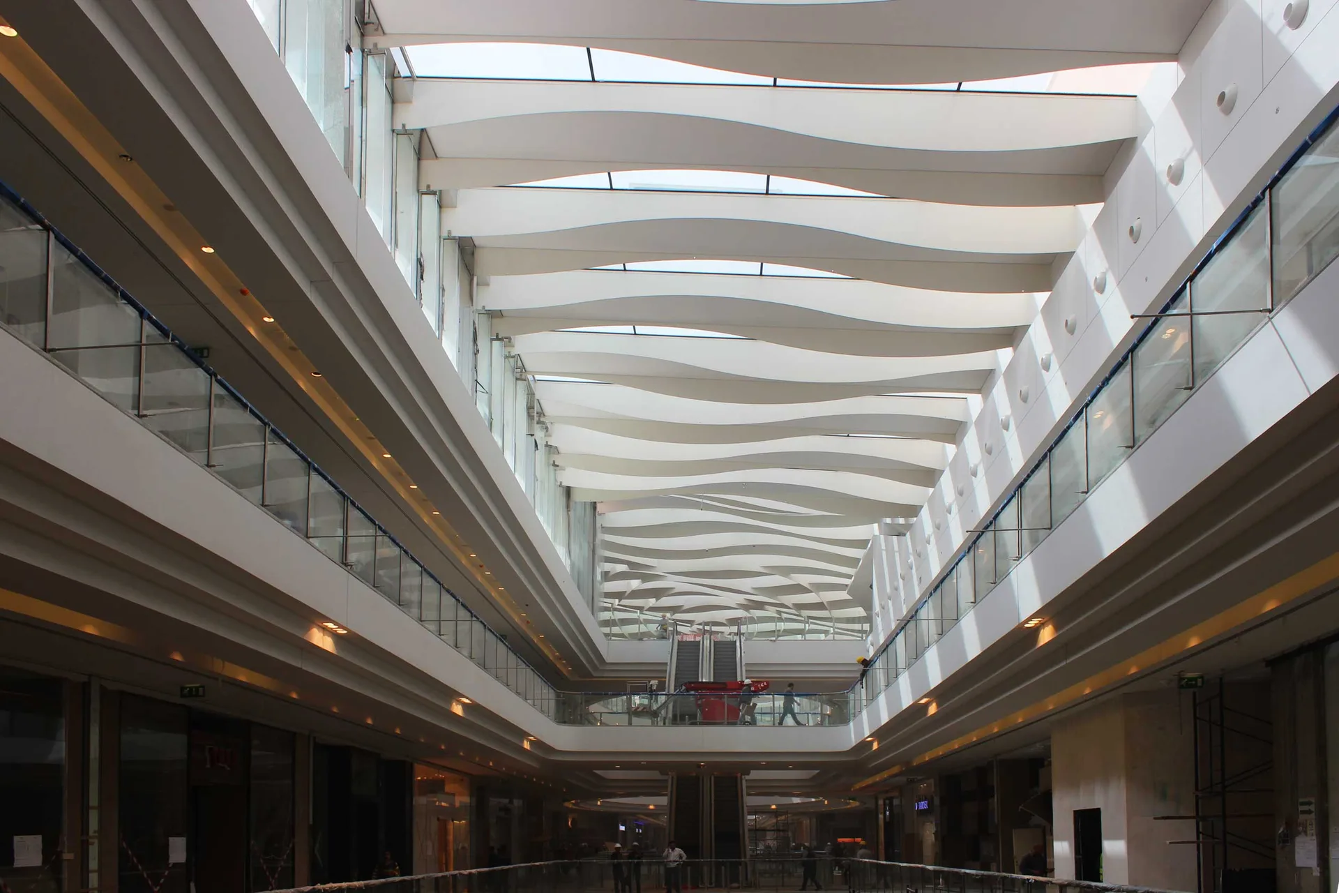 Mall atrium under a sculpted wave-blade ceiling running the length of the galleria