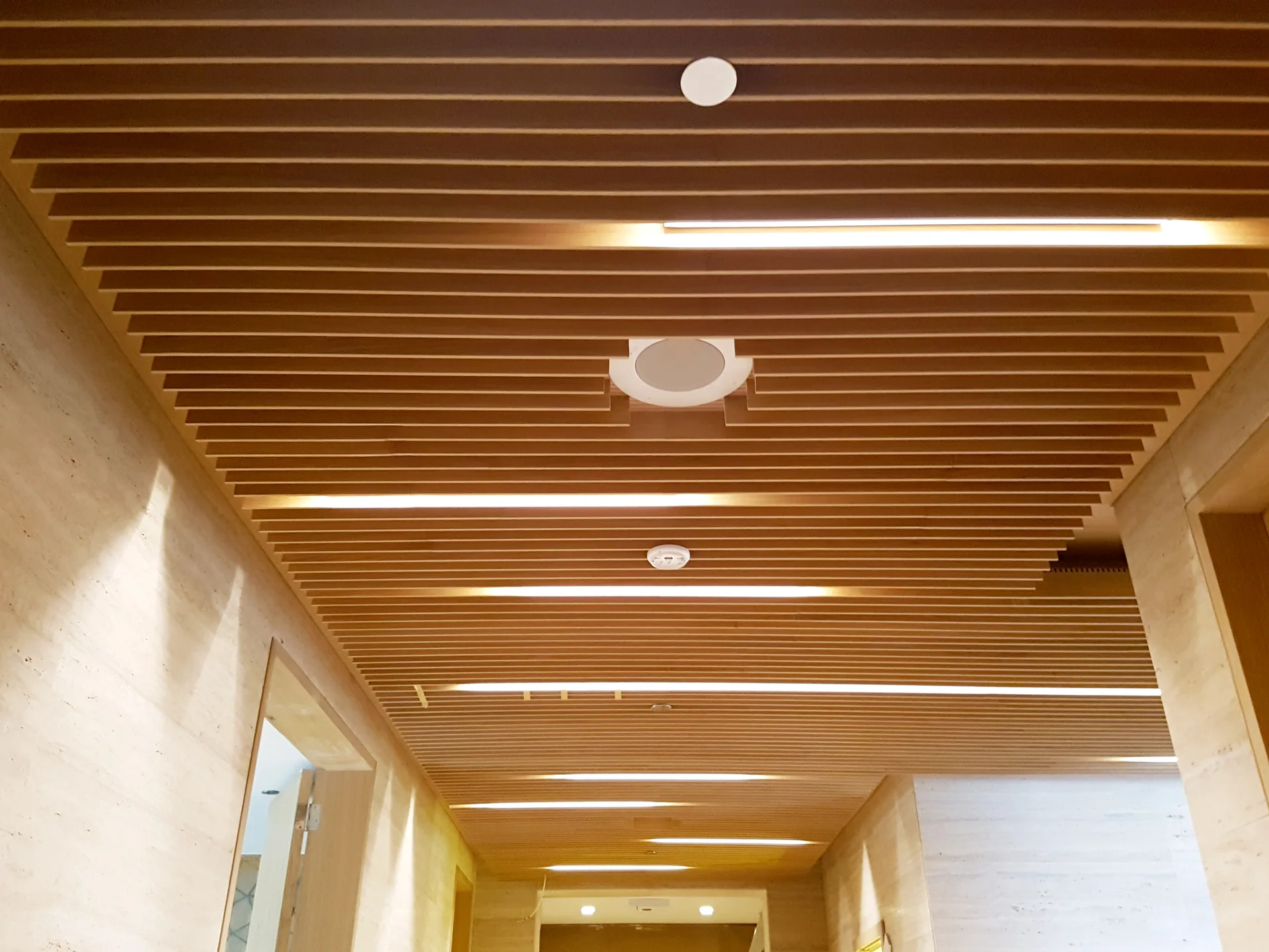 Timber batten ceiling running the length of a travertine-lined corridor