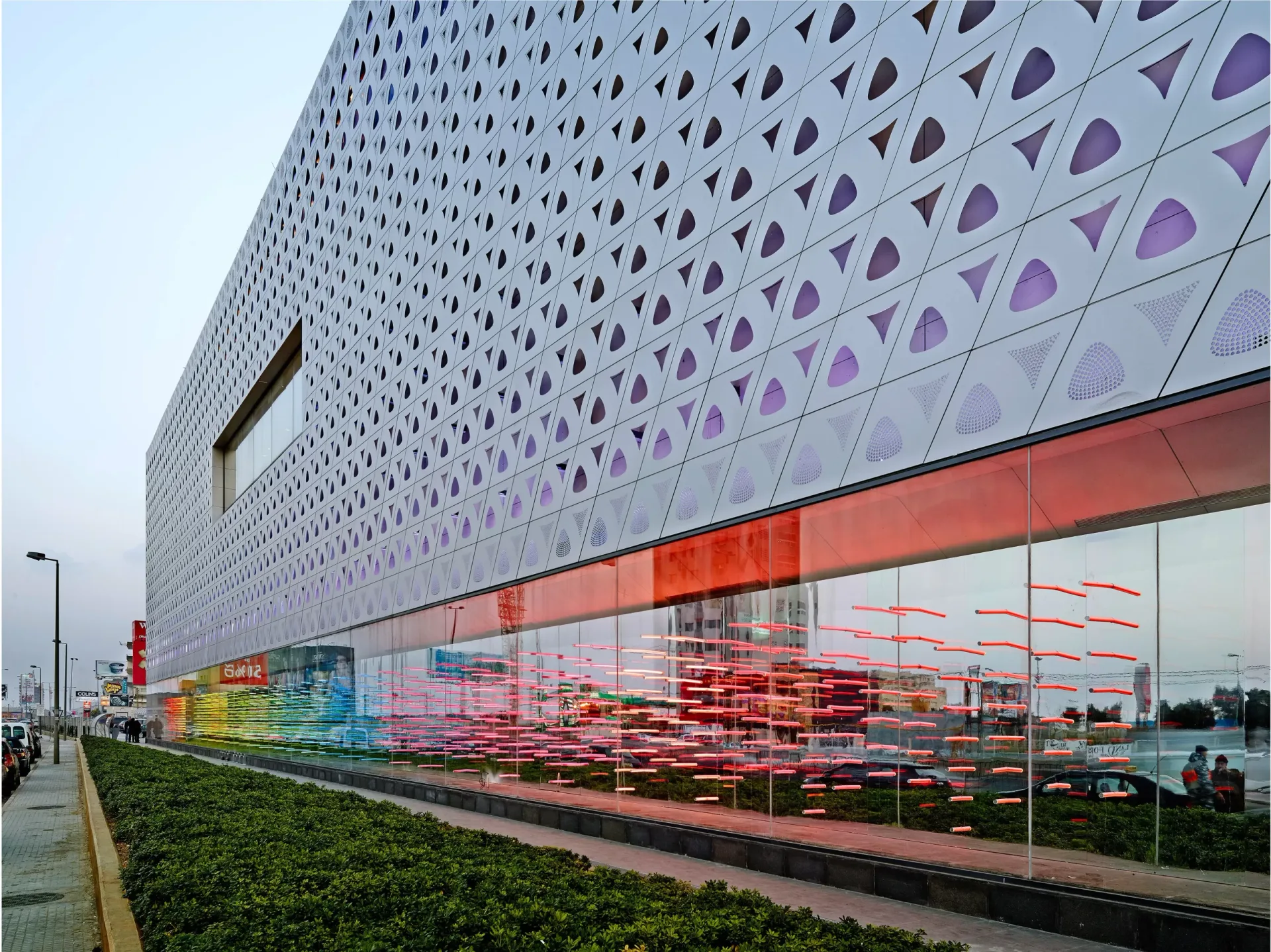 ABC Dbayeh — perforated white facade panels above a colour-glazed shopfront at dusk