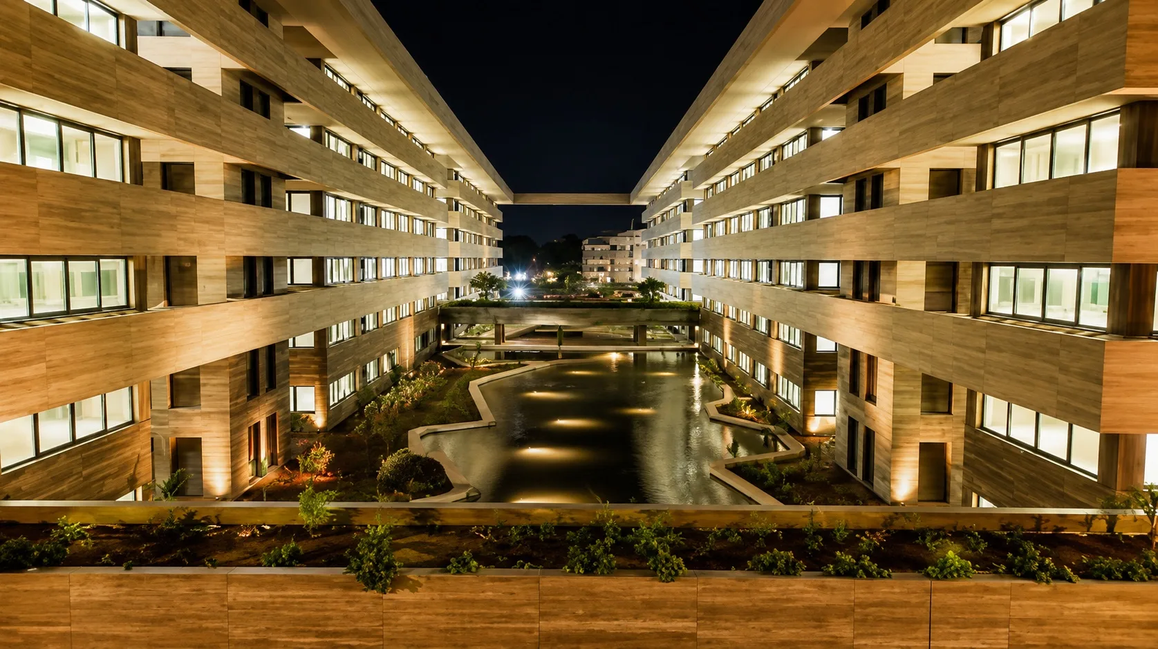 The internal courtyard at night — lit stone facades framing a landscaped water channel