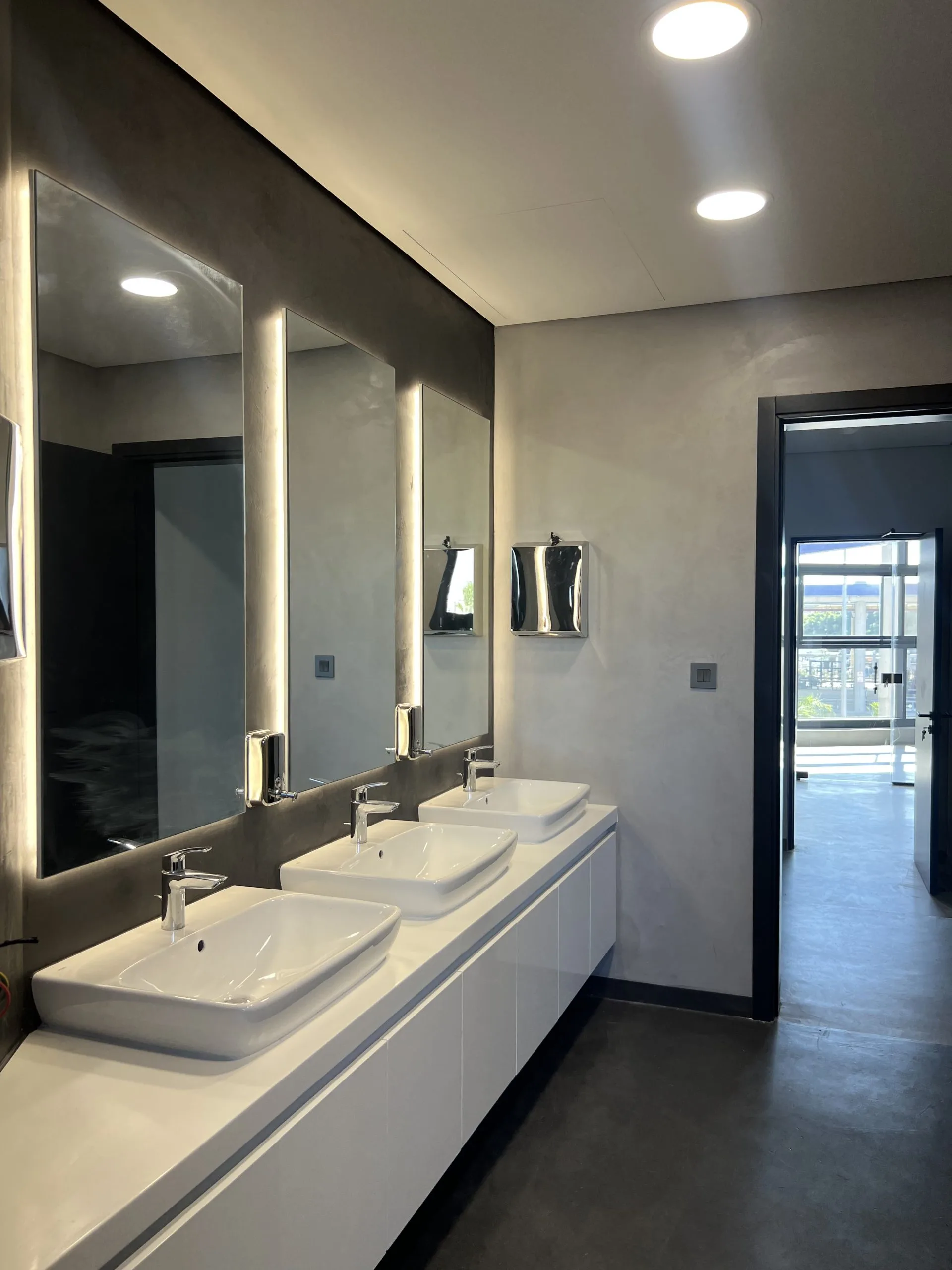Washroom — backlit mirrors above a run of white basins on a fitted vanity
