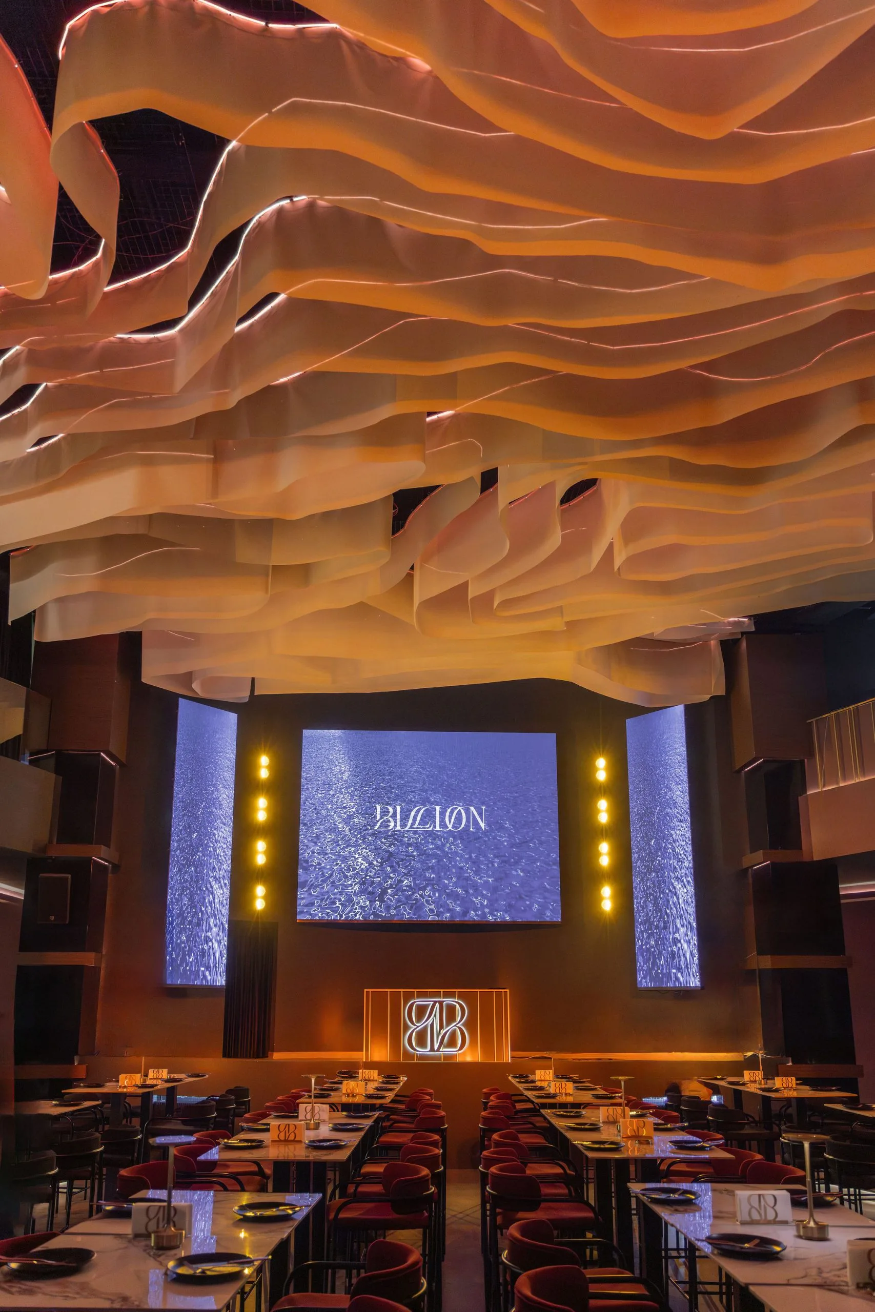 Main hall — sculpted ribbon ceiling above the dining tables and the stage screen