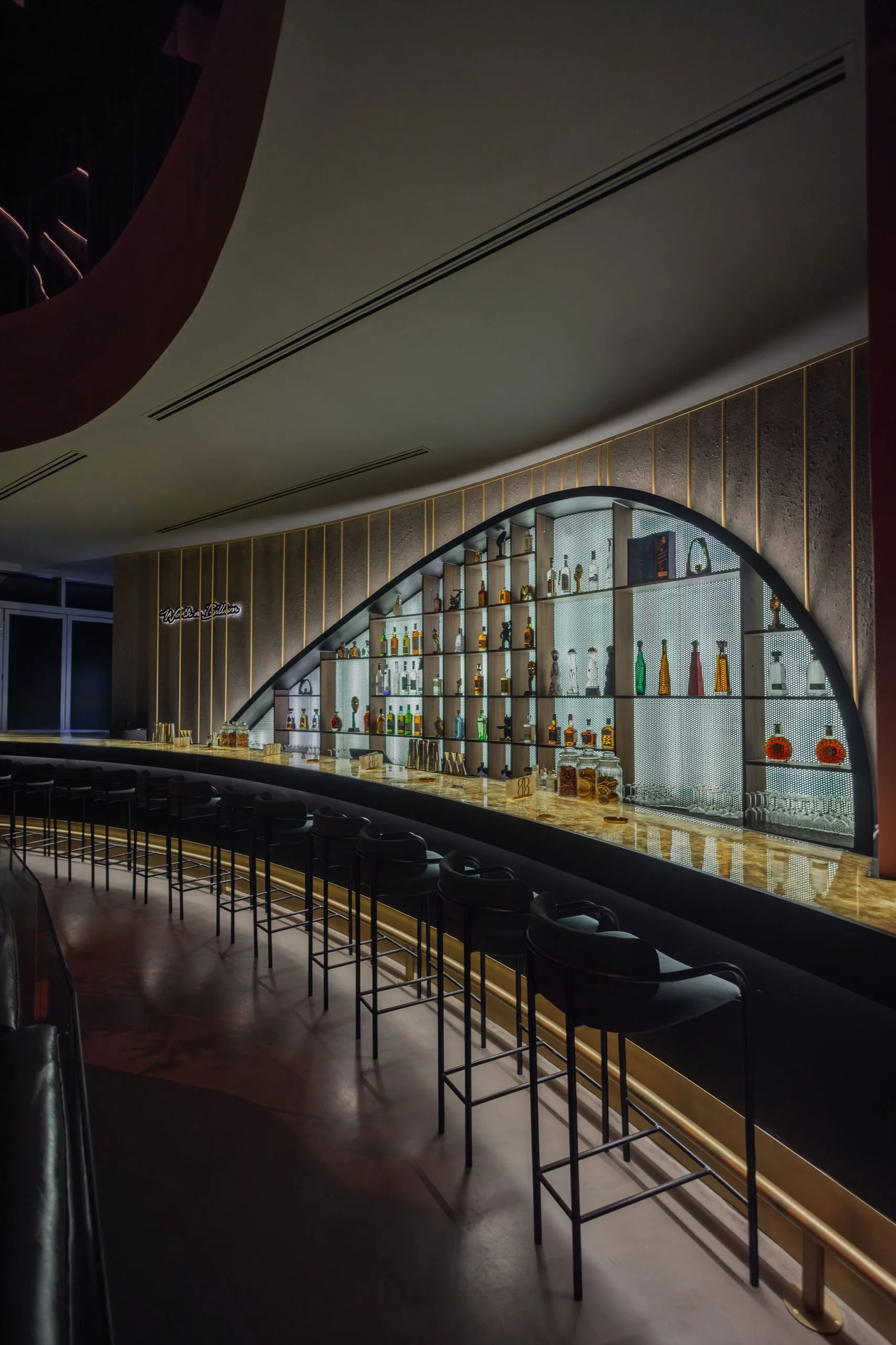 Bar seating along the sweep of the counter, arched display wall behind