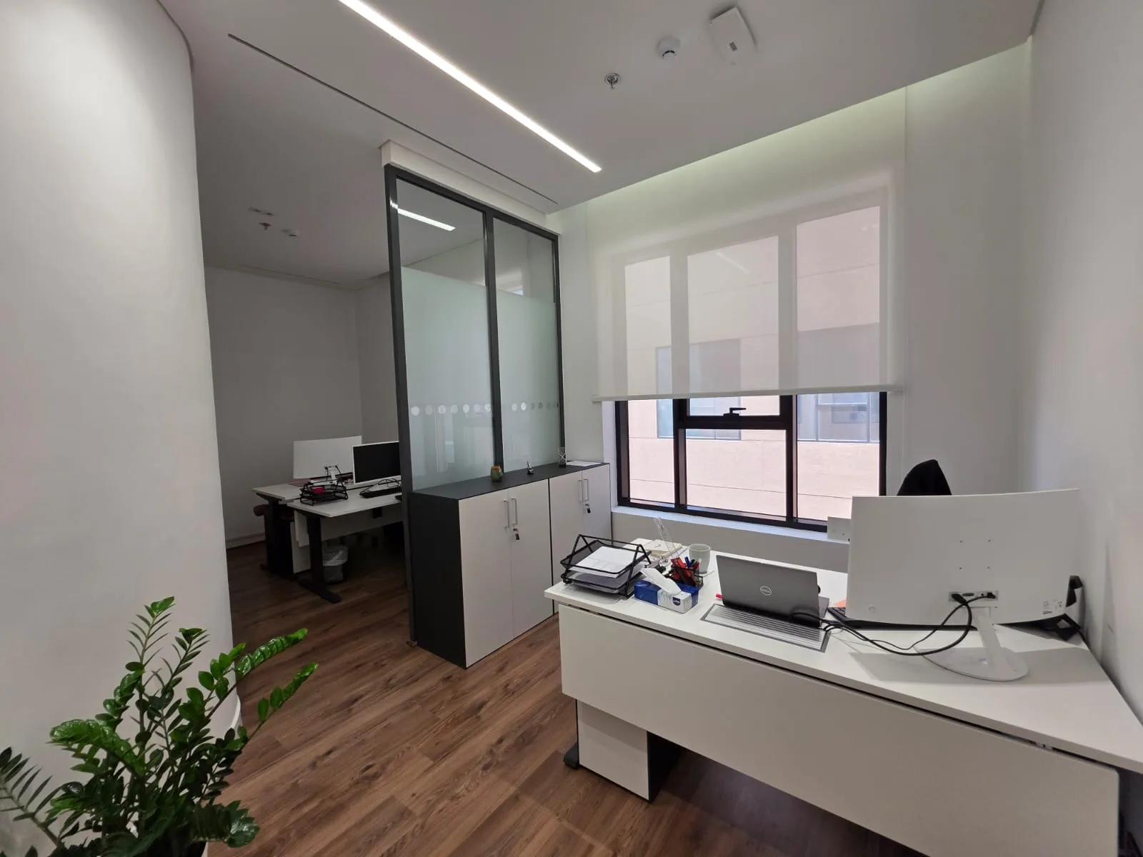Private office with a glazed partition to the adjoining room and roller blinds at the window