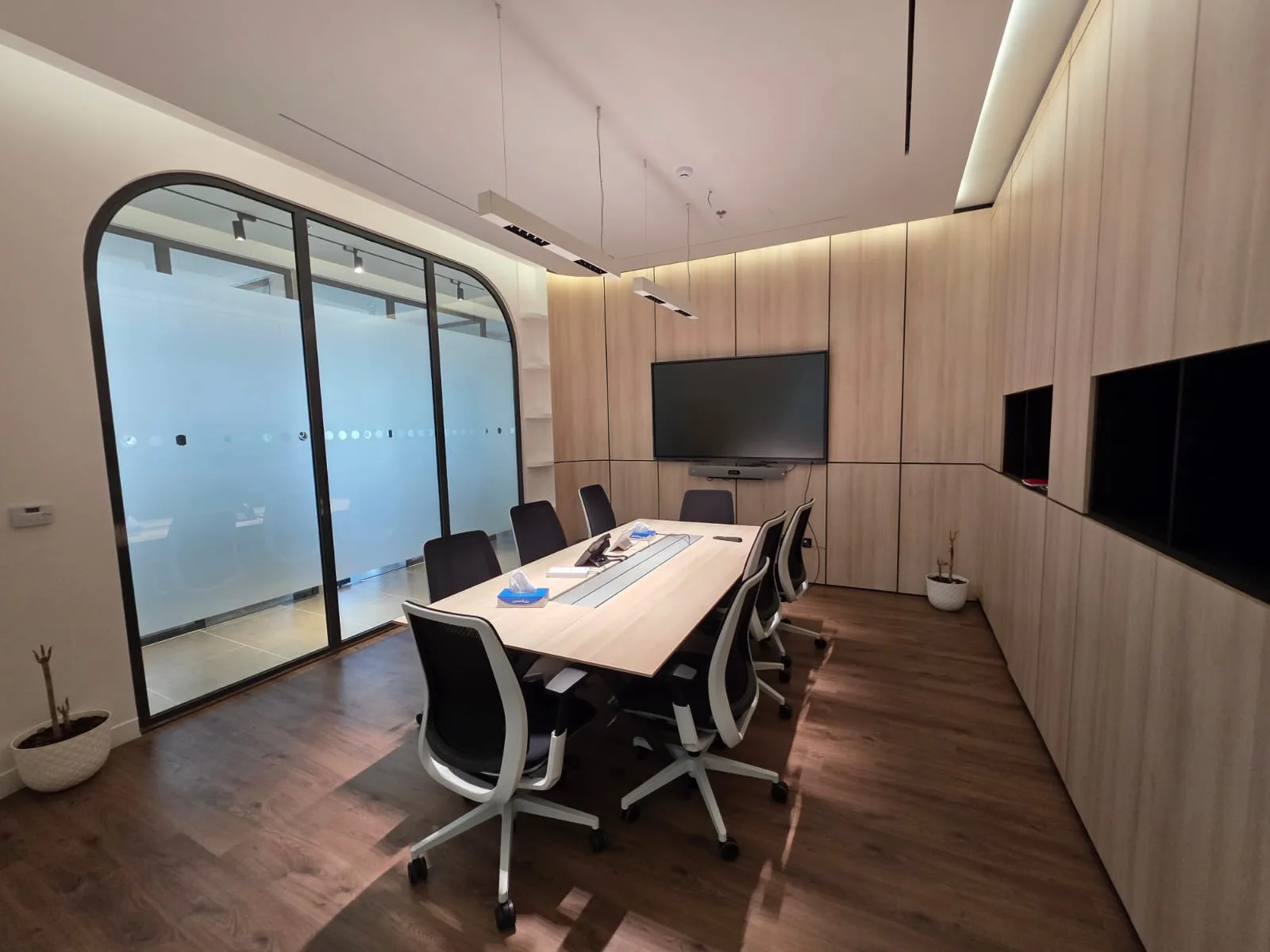 Boardroom lined in pale timber, with an arched glass partition and wall-mounted screen